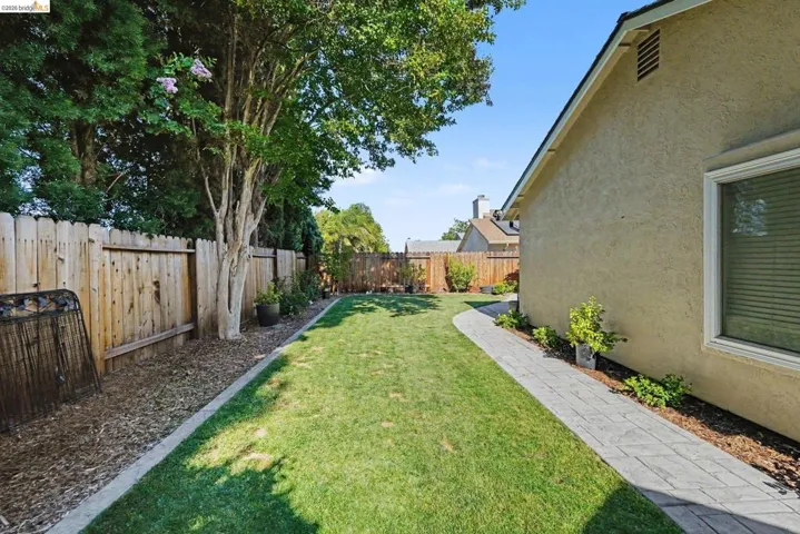 Grassed yard featuring a paver pathway, stucco exterior, perimeter fencing, and mature landscaping