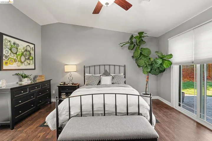 Bedroom featuring a vaulted ceiling with a ceiling fan, wood-finish flooring, and a sliding glass door leading to an exterior patio