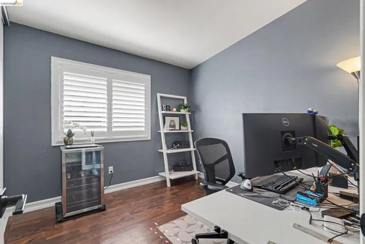 Room featuring wood-finish flooring, white baseboards, and a window with white plantation shutters