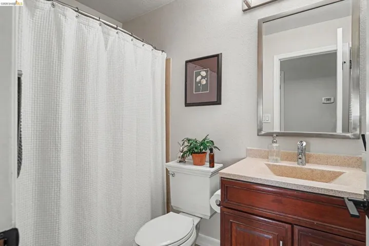 Bathroom featuring a shower with a white waffle-texture curtain, a wood-finish vanity with an integrated sink and light-colored countertop, a chrome faucet, and a rectangular mirror with a brushed metal frame