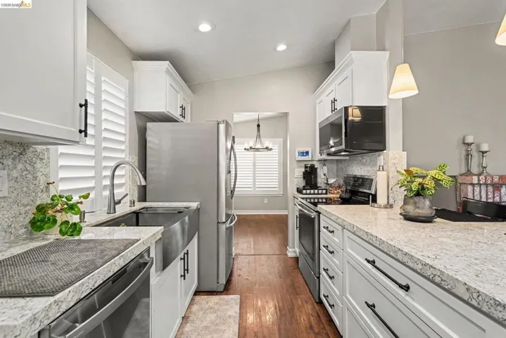 Modern kitchen featuring white shaker cabinetry, stainless steel appliances, speckled countertops, and a farmhouse sink