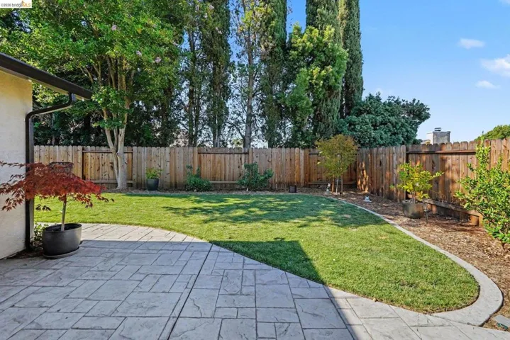 Expansive backyard featuring a stamped concrete patio, manicured lawn, and mature privacy fencing