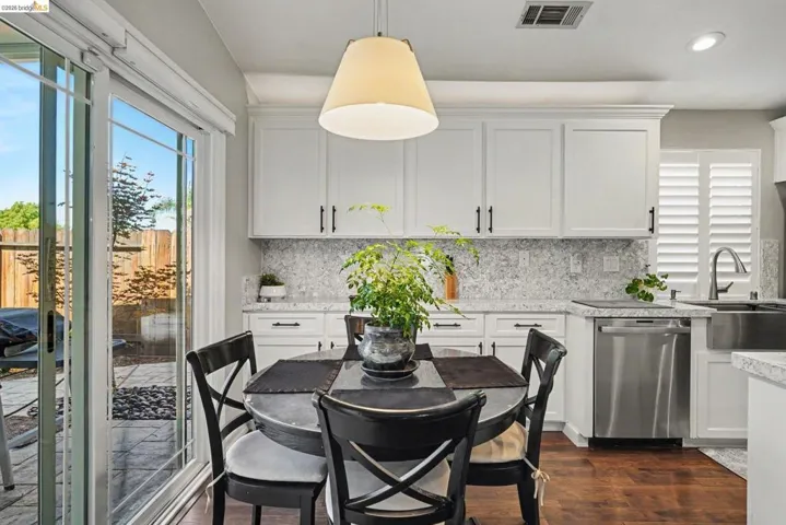 Gourmet kitchen with white cabinetry, stainless steel dishwasher, and stone countertops extending to a full backsplash