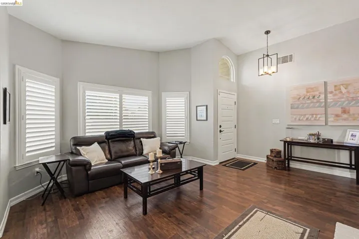 Vaulted ceilings with a geometric chandelier, wood-finish flooring, plantation shutters, and a front entry door with an arched transom window