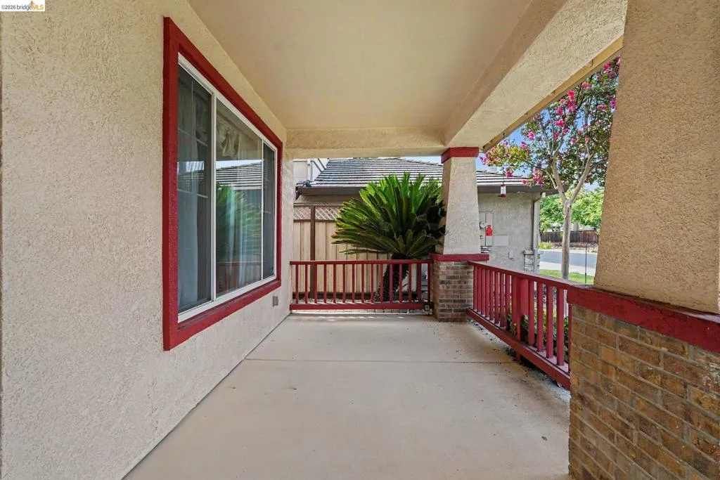 Covered front porch featuring stucco exterior, red trim accents, brick base columns, and red wood railing