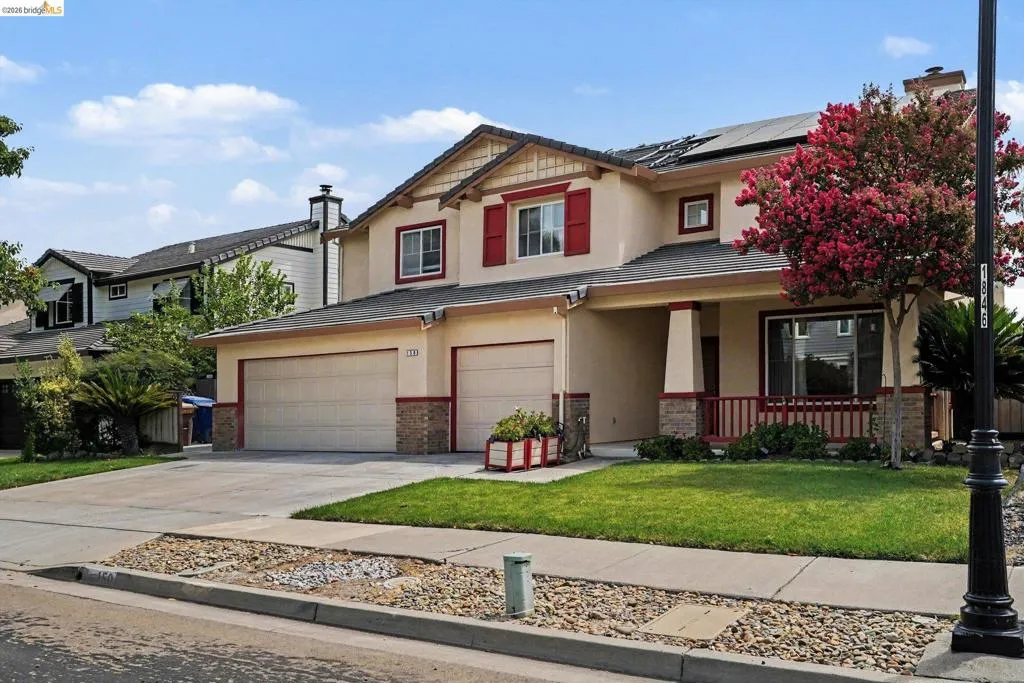 Stucco exterior featuring red window shutters, a front porch with red railings, a two-car garage, and solar panels