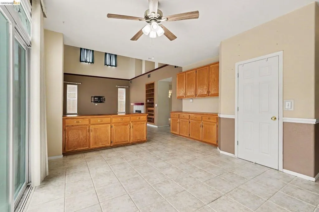 Spacious room featuring light-toned tile flooring, a ceiling fan, and built-in wood cabinetry with both upper and lower storage