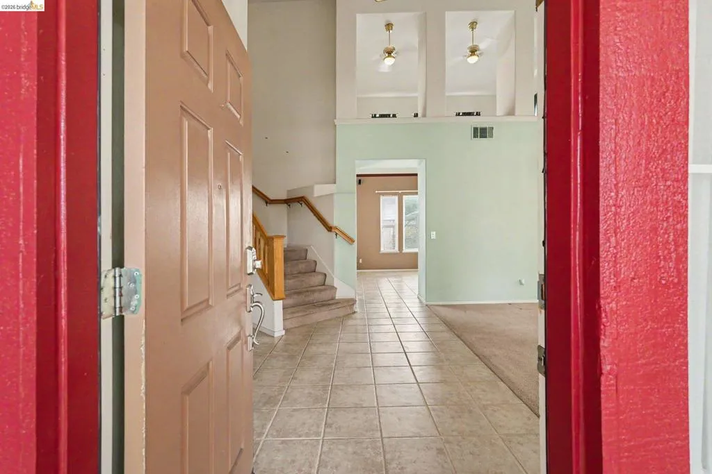 Entry foyer featuring square ceramic floor tiles and a wood-finish staircase with carpeted treads