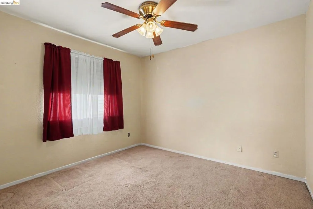 Bedroom featuring a ceiling fan with integrated lighting, a window with sheer and opaque drapery, beige walls, and carpet flooring