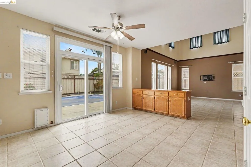 Open-concept interior featuring tile flooring, a built-in wood cabinet with storage, a ceiling fan, and sliding glass doors leading to an outdoor area with a visible pool