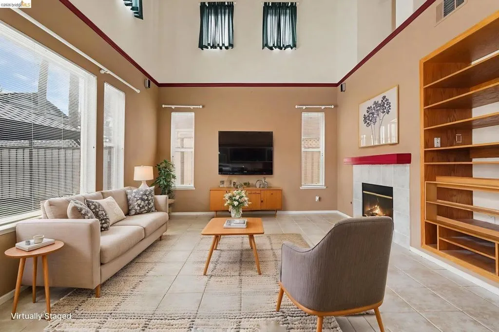 Spacious living area featuring high ceilings, tile flooring, a fireplace with a tiled surround, a built-in shelving unit, and multiple windows providing natural light