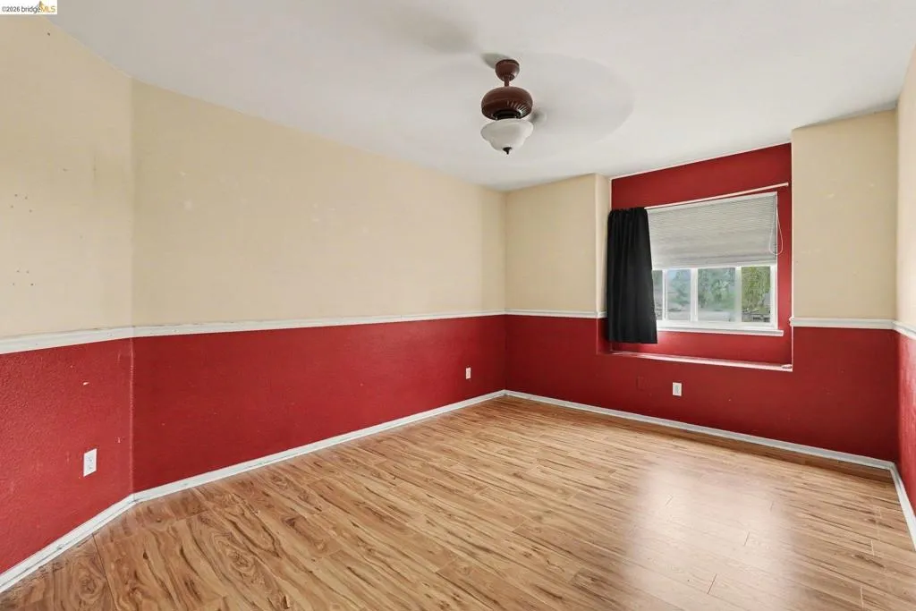 Room featuring wood-finish flooring, a ceiling fan with light fixture, and a window with a sill