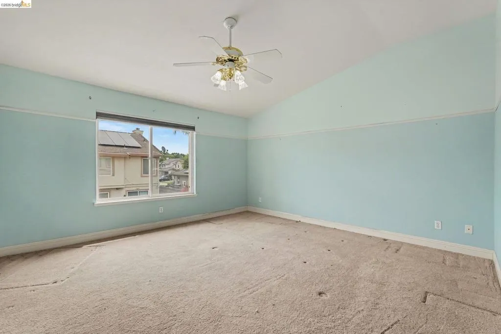 Spacious room featuring vaulted ceilings, a large window, a ceiling fan with integrated lighting, and light blue walls with white trim