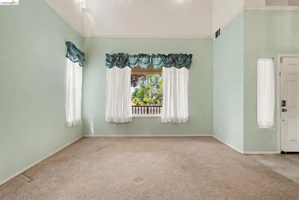 Vaulted ceiling room with broad windows, carpet flooring, and a single entry door