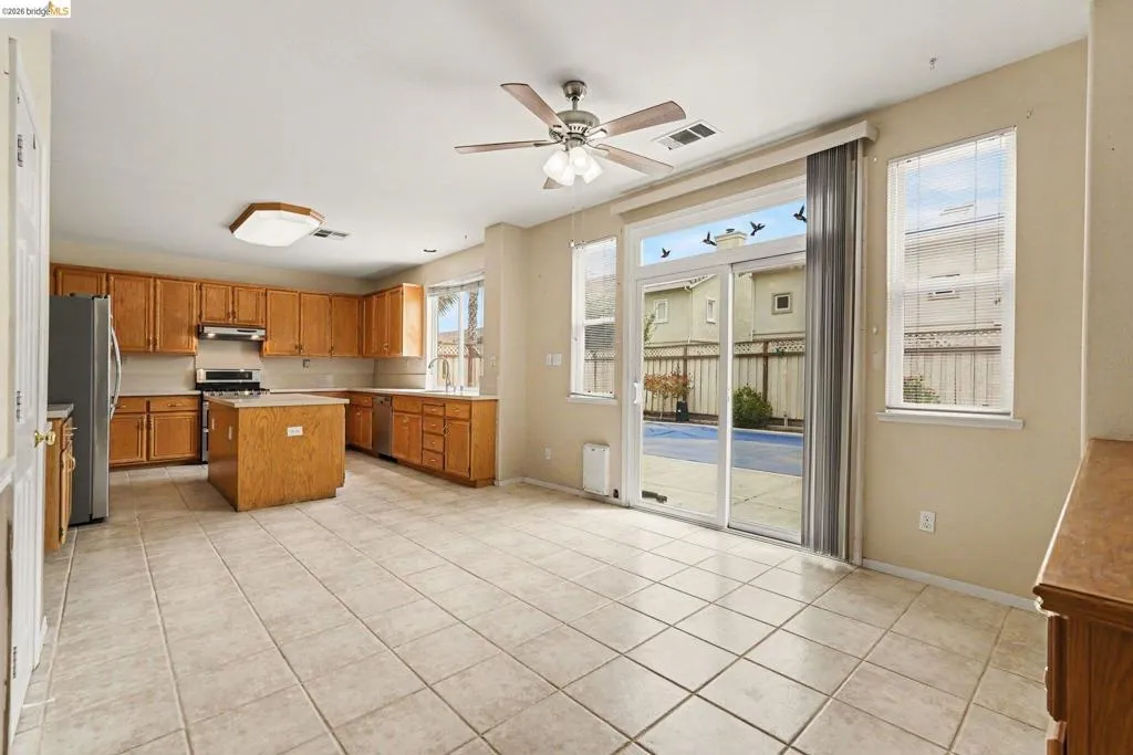 Open-concept kitchen and dining area featuring tile flooring, wooden cabinetry, a kitchen island, and stainless steel appliances