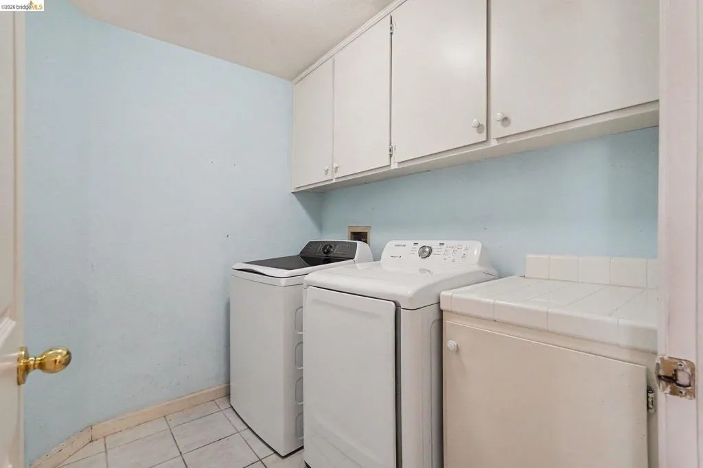 Dedicated laundry area featuring upper white cabinetry, a white tiled countertop, and neutral tile flooring