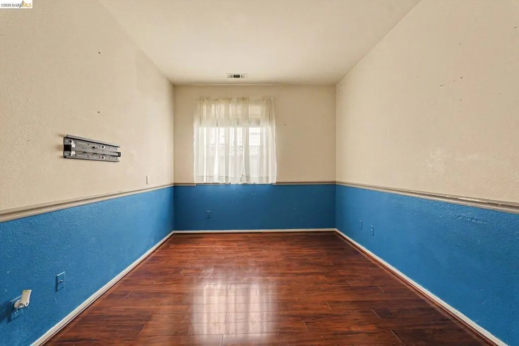 Spacious room featuring wood-finish flooring, two-tone wall treatment with a chair rail, and a window with sheer curtains