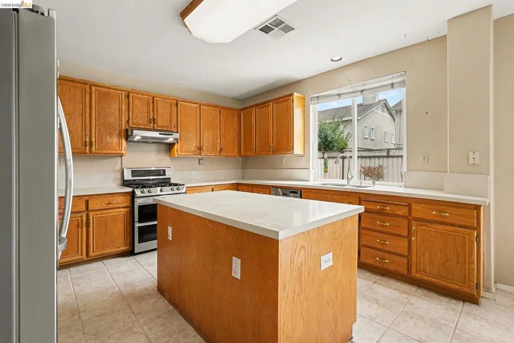 Kitchen featuring a central island with a light-toned countertop, extensive wood cabinetry, tile flooring, and a stainless steel gas range with a matching range hood