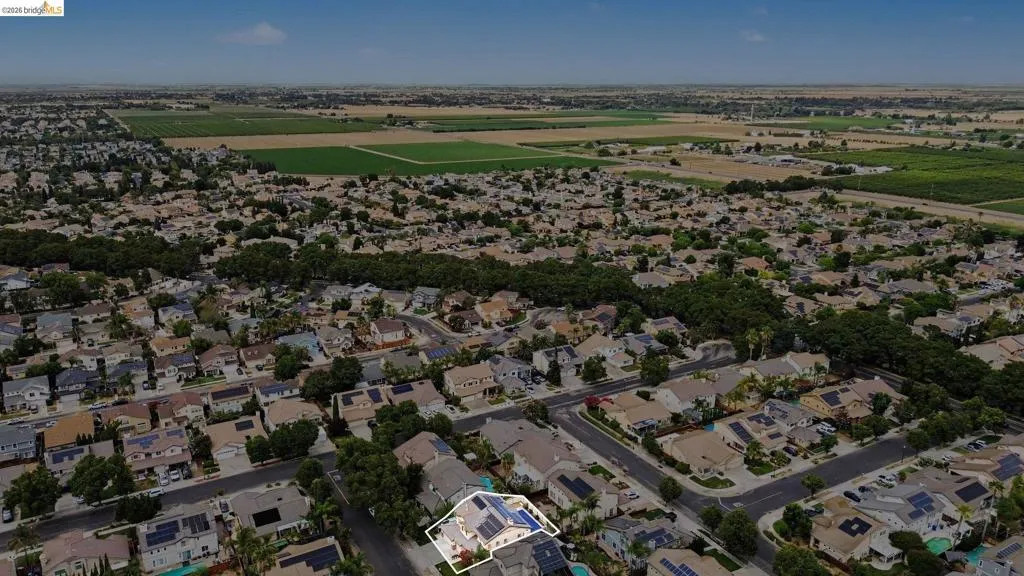 Aerial perspective of a residential neighborhood with a highlighted property featuring a light-colored exterior, an attached garage, and a fenced backyard