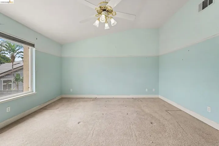 Room featuring vaulted ceilings, a window with exterior views, light blue and white two-tone walls, a ceiling fan with light fixture, and carpeted flooring