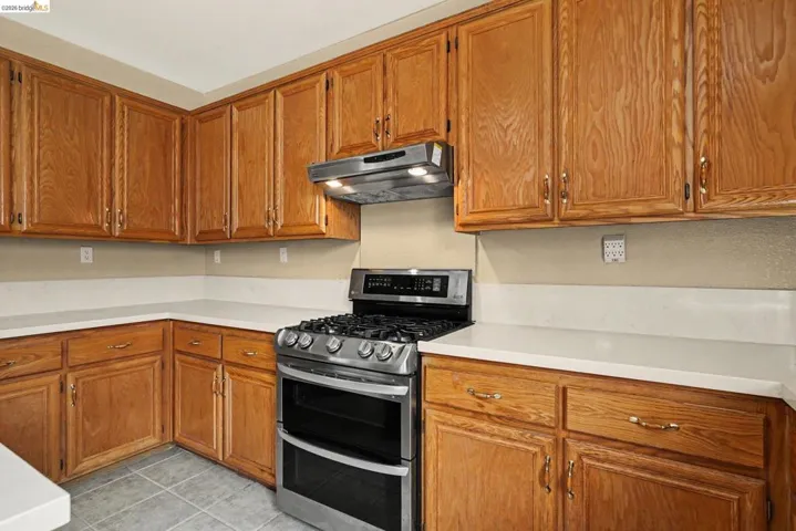 Kitchen featuring abundant wood cabinetry, light-toned countertops, a stainless steel gas range with a double oven, a coordinating range hood, and tile flooring