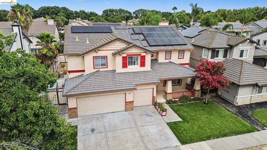 Two-story stucco home featuring a tile roof, solar panels, an attached two-car garage, and a manicured front lawn