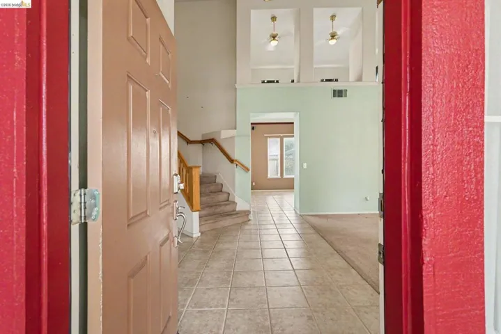 Entry foyer featuring square ceramic floor tiles and a wood-finish staircase with carpeted treads