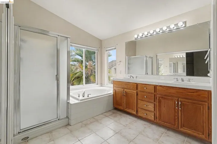 Bathroom featuring a built-in soaking tub, a separate glass-enclosed shower, a double vanity with wood cabinetry, tile countertops, and tile flooring