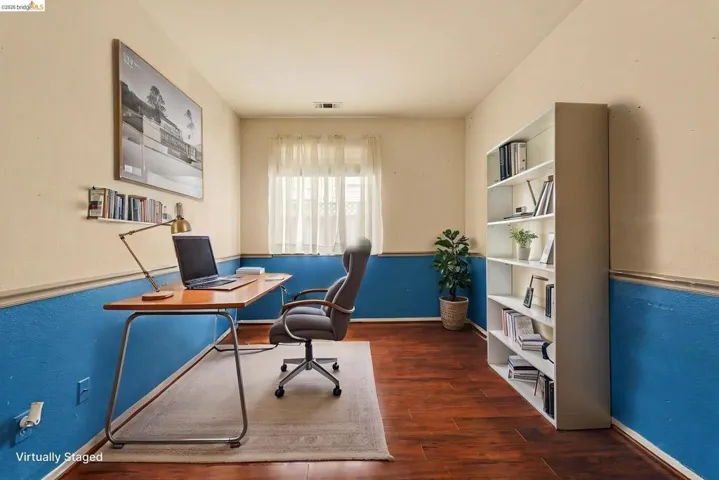Room featuring wood-finish flooring, a window with sheer curtains, and a built-in shelving unit