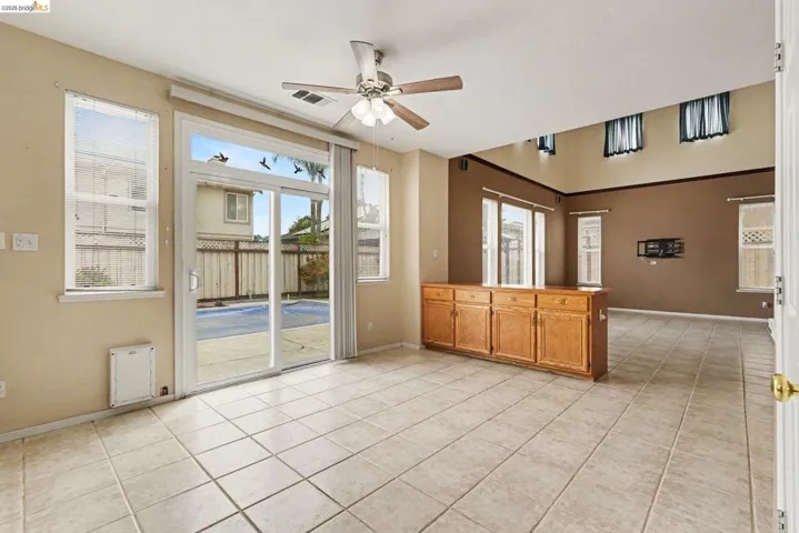 Open-concept interior featuring tile flooring, a built-in wood cabinet with storage, a ceiling fan, and sliding glass doors leading to an outdoor area with a visible pool