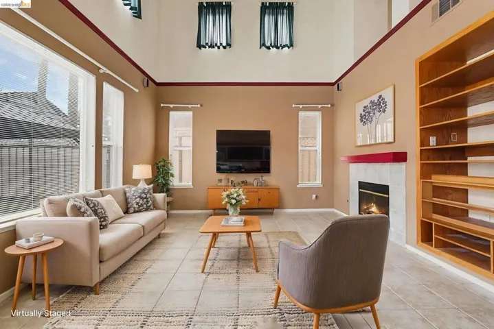 Spacious living area featuring high ceilings, tile flooring, a fireplace with a tiled surround, a built-in shelving unit, and multiple windows providing natural light