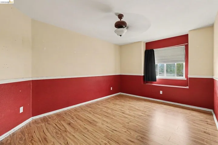 Room featuring wood-finish flooring, a ceiling fan with light fixture, and a window with a sill