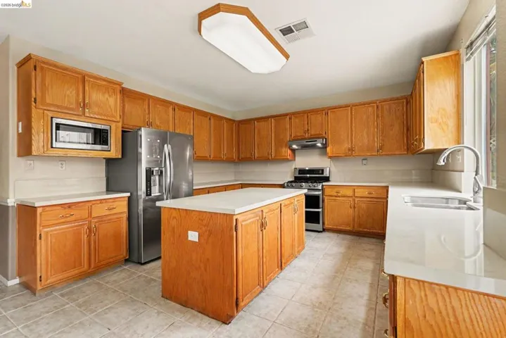 Spacious kitchen featuring extensive wood cabinetry, light-toned countertops, tile flooring, a central island, and stainless steel appliances including a range and refrigerator