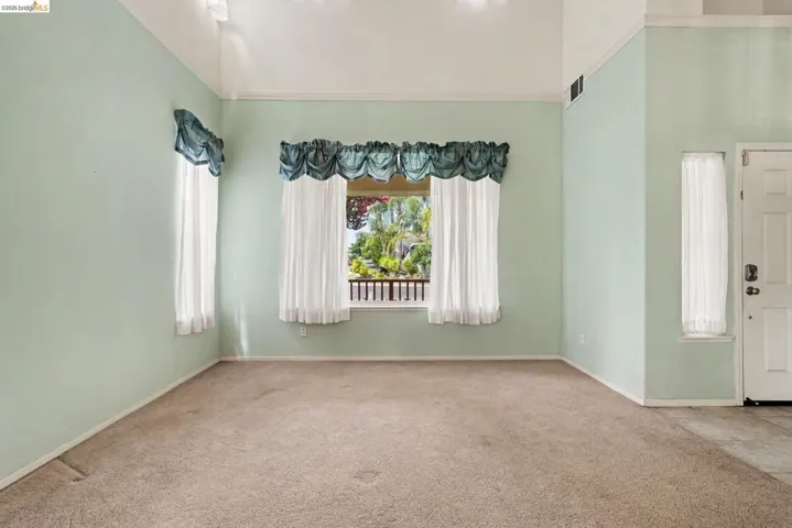 Vaulted ceiling room with broad windows, carpet flooring, and a single entry door