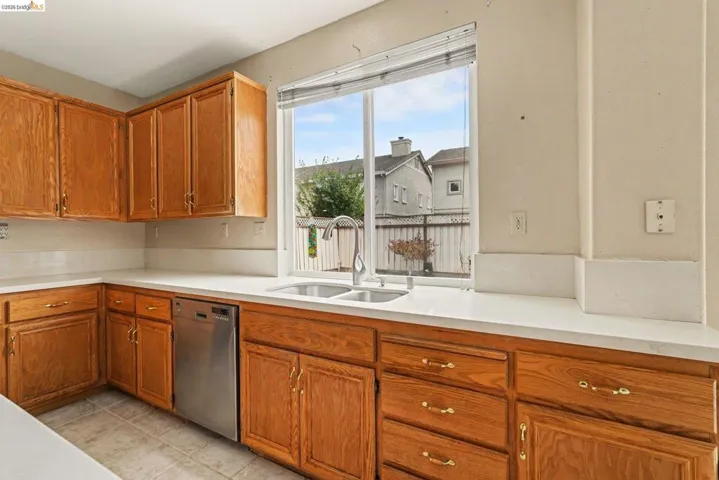 Bright kitchen featuring a double basin sink with a gooseneck faucet, light-toned countertops, and ample cabinetry with brass-toned hardware