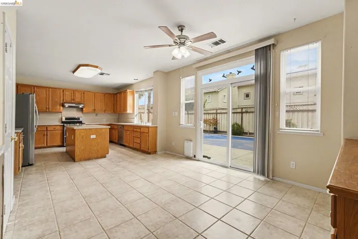Open-concept kitchen and dining area featuring tile flooring, wooden cabinetry, a kitchen island, and stainless steel appliances