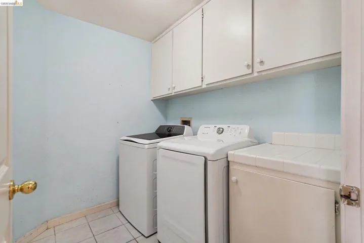 Dedicated laundry area featuring upper white cabinetry, a white tiled countertop, and neutral tile flooring