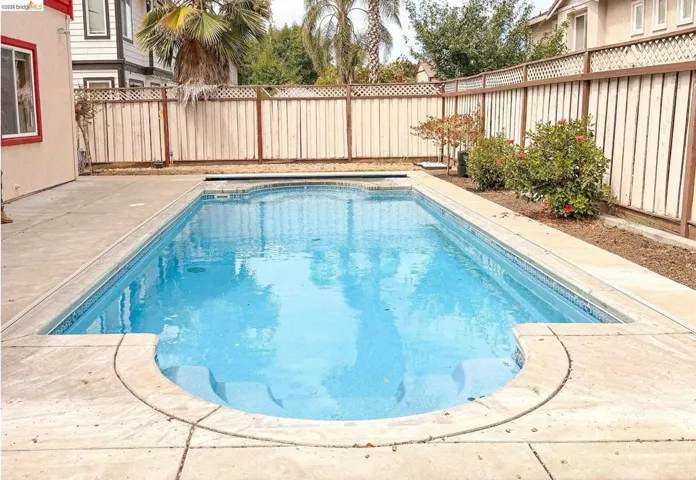 In-ground swimming pool featuring a curved entry, concrete decking, and perimeter landscaping