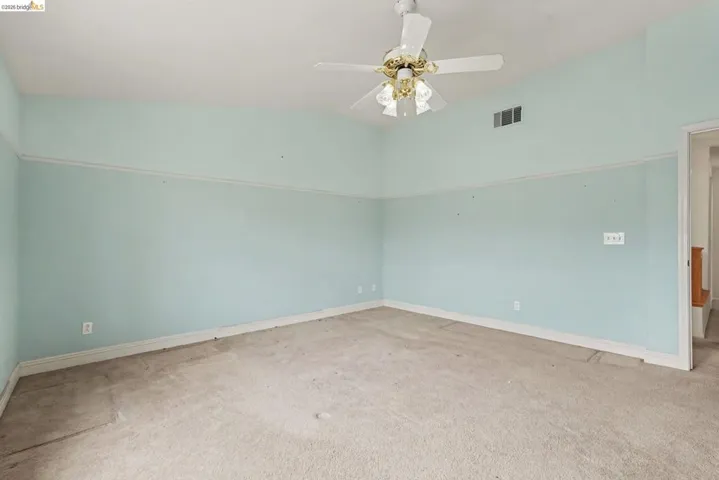 Spacious room featuring a vaulted ceiling with a ceiling fan, light blue walls with white trim, and carpeted flooring
