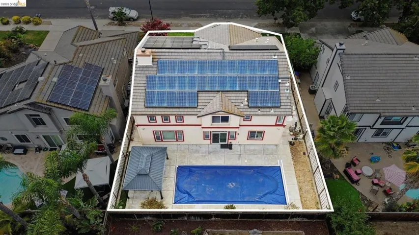 Rear exterior featuring a covered swimming pool, extensive paved patio, and a gazebo