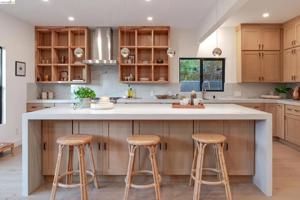Kitchen featuring light wood-finish cabinetry, a waterfall island with a light countertop, a stainless steel range hood, and a white marble-patterned backsplash