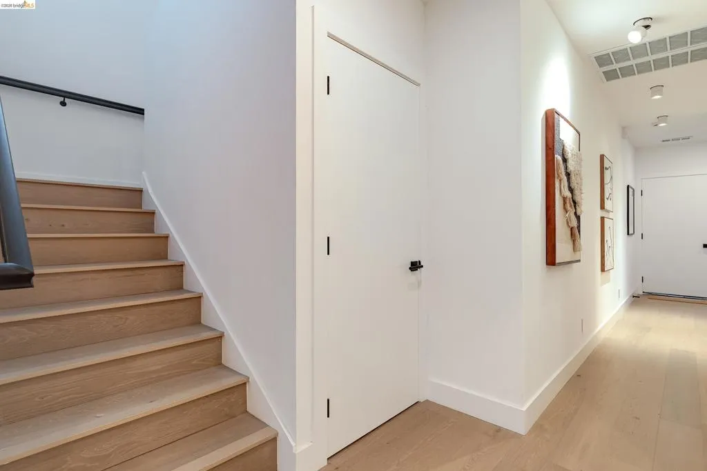 Hardwood flooring throughout the hallway and staircase, featuring a black handrail and white walls