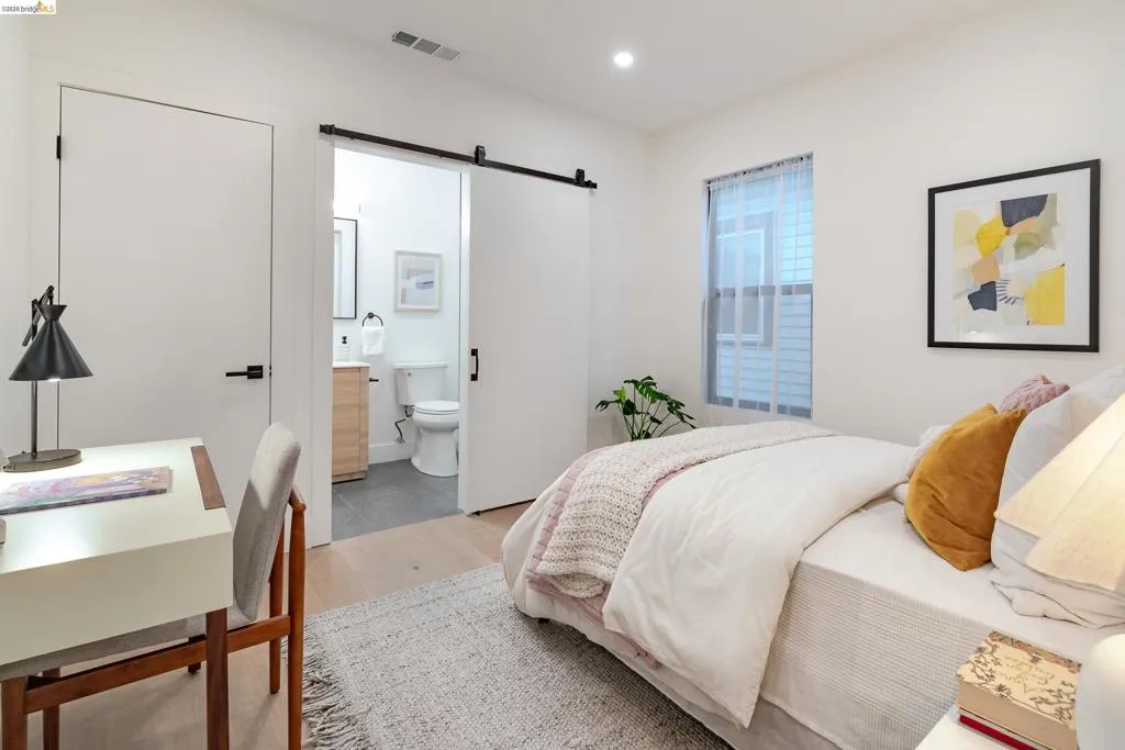 Light wood-finish flooring complements white walls, featuring a sliding barn door entry to a bathroom with a wood vanity and gray tile flooring