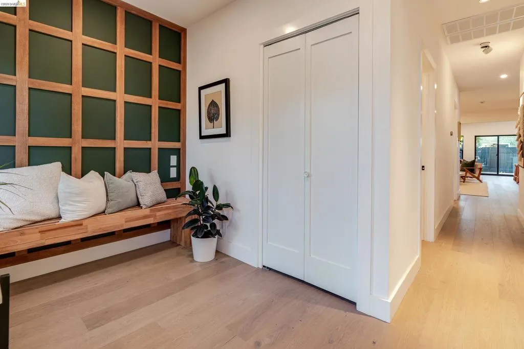 Built-in wooden bench with a grid-pattern accent wall, light wood-finish flooring, white walls, and a recessed lighting fixture