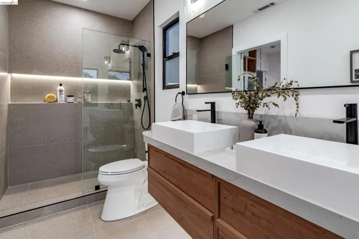 Dual vessel sinks with matte black faucets and a wood-finish vanity