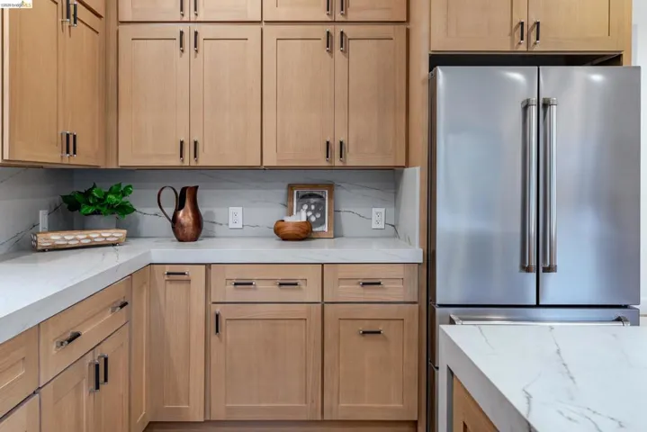 Kitchen featuring light wood cabinetry with dark hardware, a stainless steel French door refrigerator, and white countertops with veining