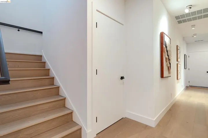 Hardwood flooring throughout the hallway and staircase, featuring a black handrail and white walls