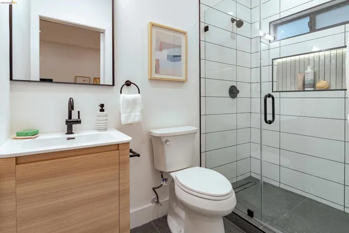 Bathroom featuring a glass-enclosed shower with a tiled surround, a wood-finish vanity with an integrated sink, a dark-finish faucet, and a wall-mounted mirror