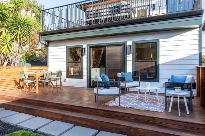 Expansive wood-finish deck with multiple seating areas, a sliding glass door, and dark-framed windows