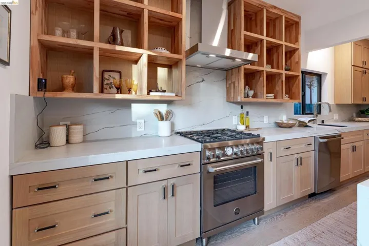 Gourmet kitchen featuring a stainless steel range and hood, light wood cabinetry, white countertops, and a white marble-look backsplash